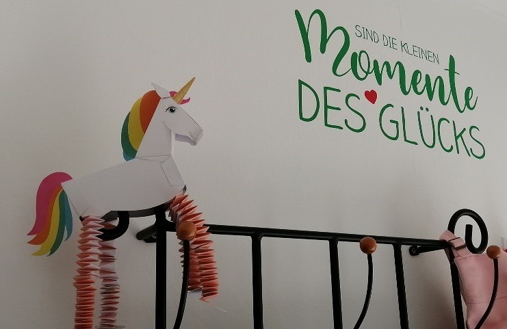 Praxiswand mit dem Schriftzug „Sind die kleinen Momente des Glücks“, einem gebastelten Papier-Einhorn und einer Garderobe