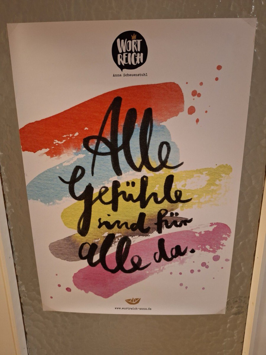 Plakat in der Praxis Finster mit dem handgeschriebenen Satz „Alle Gefühle sind für alle da“ auf bunten Aquarellflächen